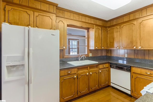 kitchen featuring white appliances, dark countertops, brown cabinets, and a sink