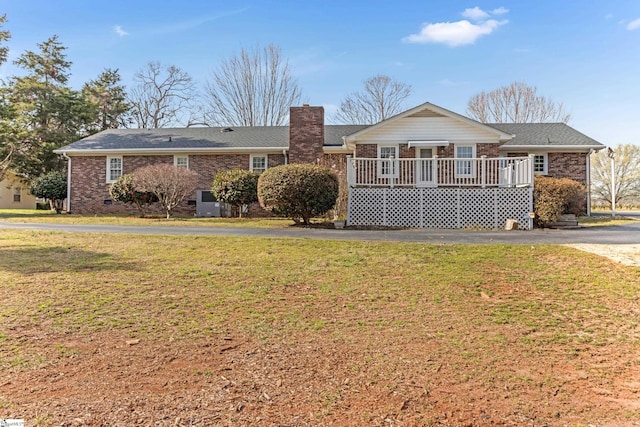 single story home featuring driveway, brick siding, a chimney, and a front lawn