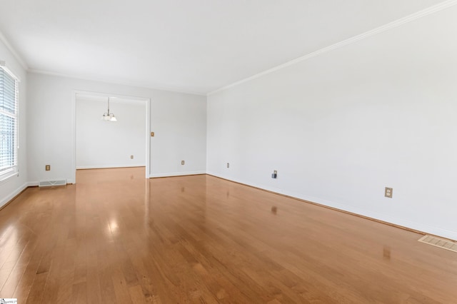 unfurnished room featuring baseboards, wood finished floors, visible vents, and ornamental molding