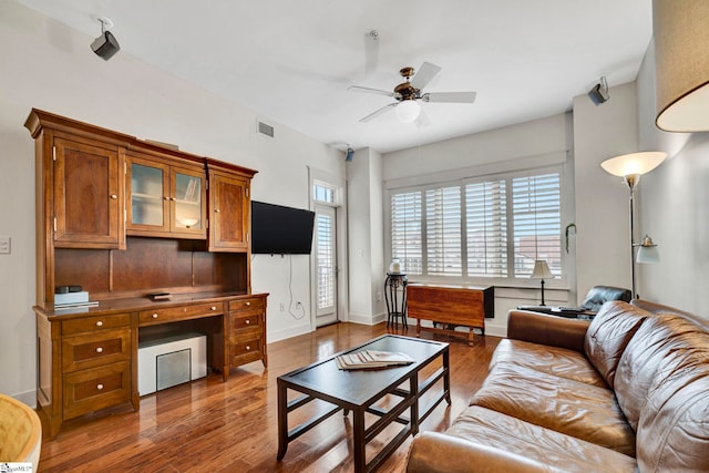 living area with baseboards, wood finished floors, visible vents, and ceiling fan