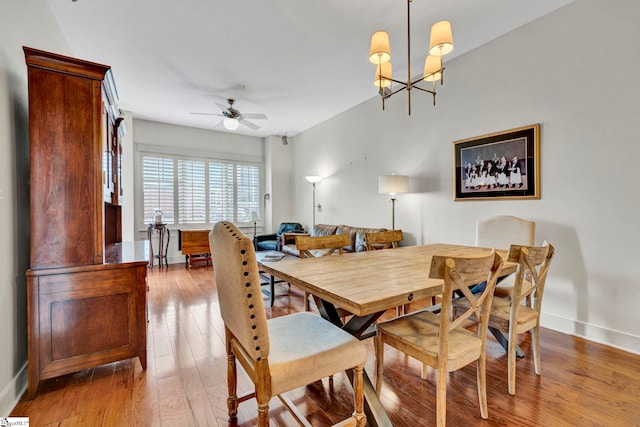 dining space featuring hardwood / wood-style floors, ceiling fan with notable chandelier, and baseboards