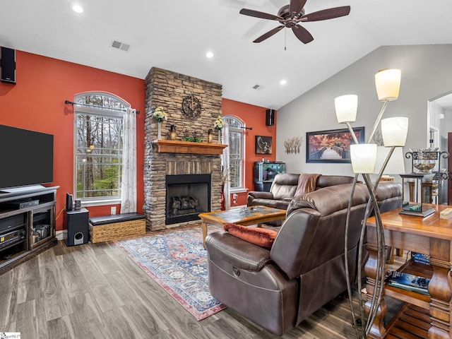 living area with visible vents, wood finished floors, a stone fireplace, lofted ceiling, and ceiling fan