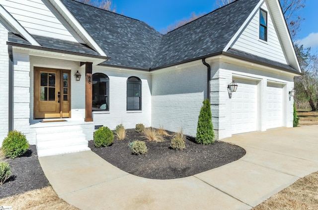 entrance to property featuring brick siding, roof with shingles, and concrete driveway