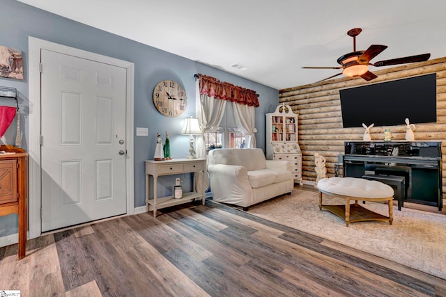 living room with log walls, wood finished floors, visible vents, and ceiling fan