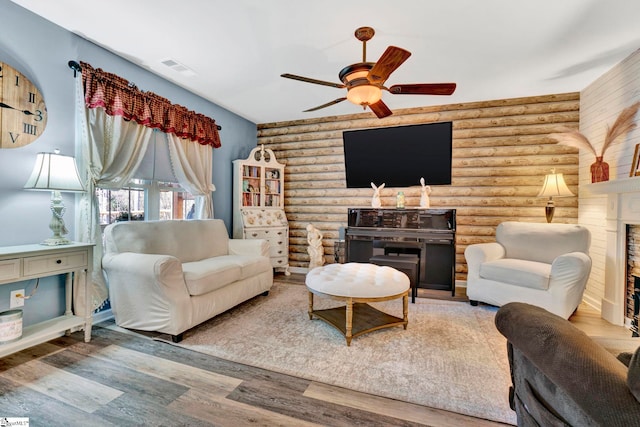 living room with rustic walls, visible vents, ceiling fan, and wood finished floors