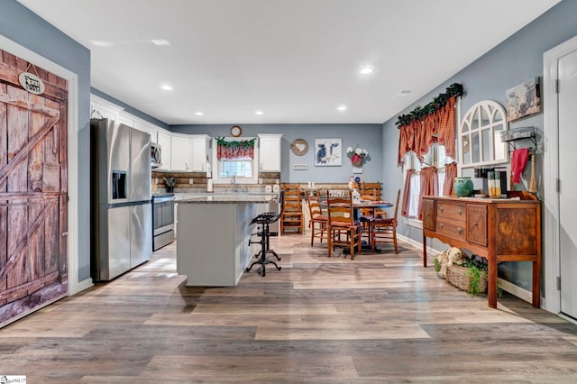 kitchen featuring a kitchen island, a breakfast bar, light wood-style flooring, appliances with stainless steel finishes, and white cabinets