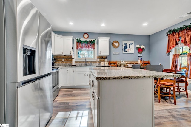 kitchen with light wood-type flooring, visible vents, a kitchen island, appliances with stainless steel finishes, and light stone countertops