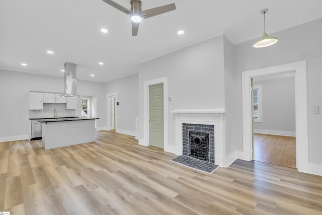 unfurnished living room with light wood-type flooring, baseboards, a ceiling fan, and a tile fireplace