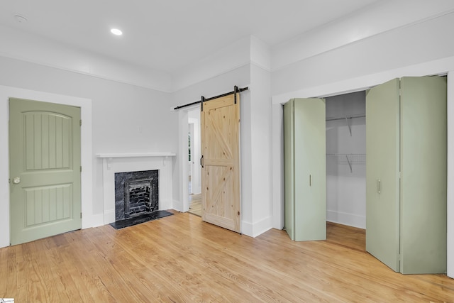 unfurnished living room featuring light wood finished floors, baseboards, a barn door, recessed lighting, and a fireplace