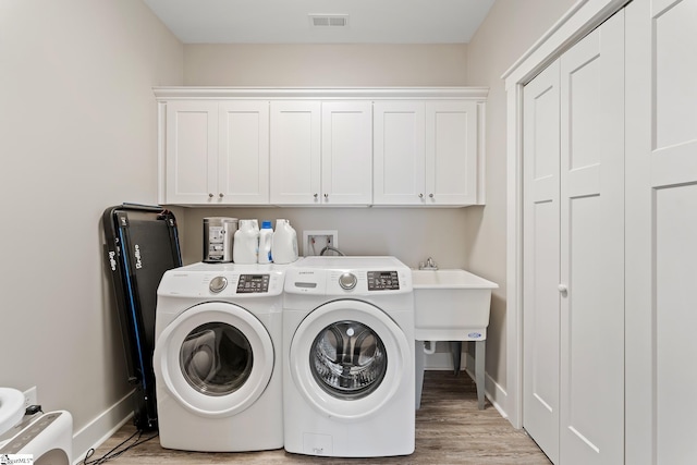 clothes washing area featuring light wood finished floors, visible vents, baseboards, washing machine and dryer, and cabinet space