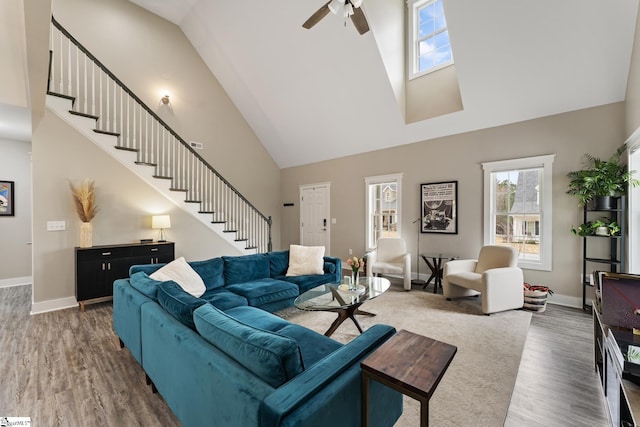 living room with a ceiling fan, wood finished floors, baseboards, a towering ceiling, and stairs