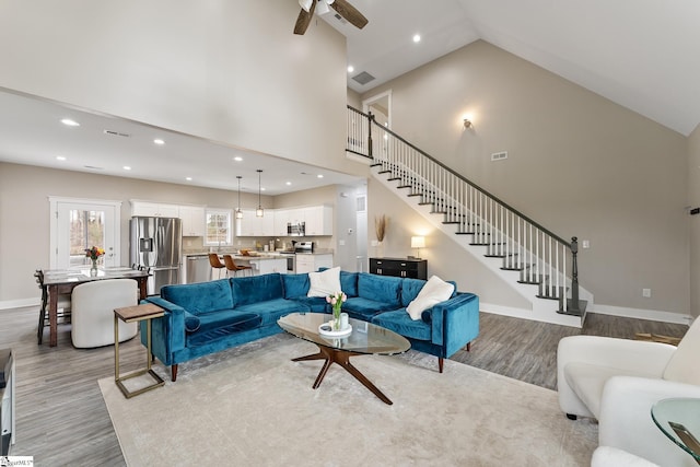 living room with stairway, high vaulted ceiling, a ceiling fan, and wood finished floors