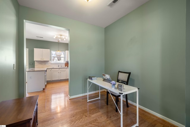 office featuring visible vents, a notable chandelier, a sink, light wood finished floors, and baseboards