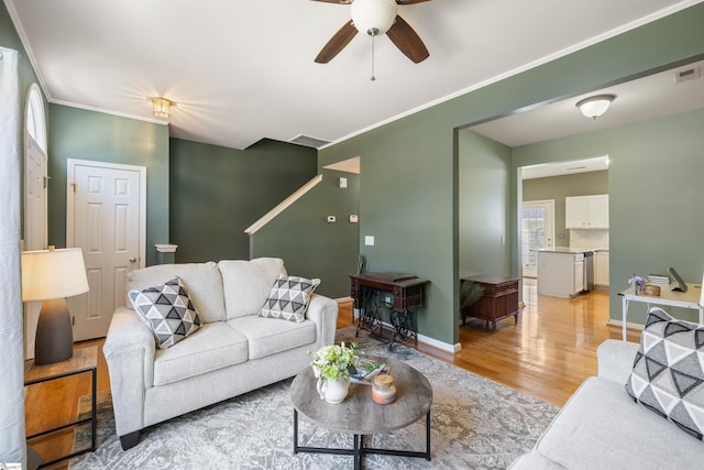 living room with visible vents, light wood-style flooring, a ceiling fan, ornamental molding, and baseboards