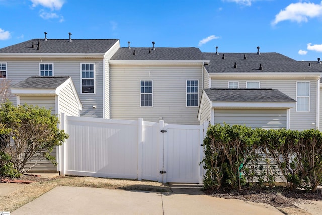 back of property featuring a gate, fence, and roof with shingles