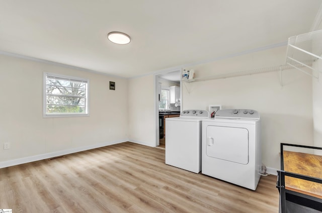 clothes washing area featuring light wood-style floors, crown molding, baseboards, laundry area, and washing machine and clothes dryer