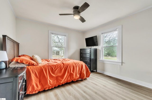 bedroom with visible vents, light wood-style flooring, a ceiling fan, ornamental molding, and baseboards