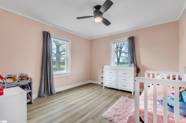 bedroom with a crib, light wood-style flooring, baseboards, and ornamental molding