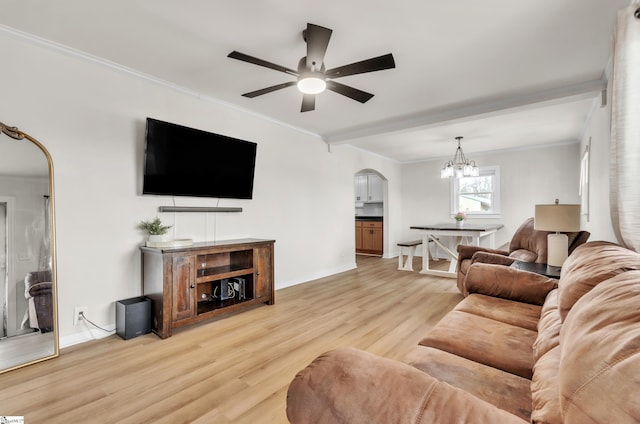 living area with baseboards, arched walkways, ornamental molding, light wood-style floors, and ceiling fan with notable chandelier