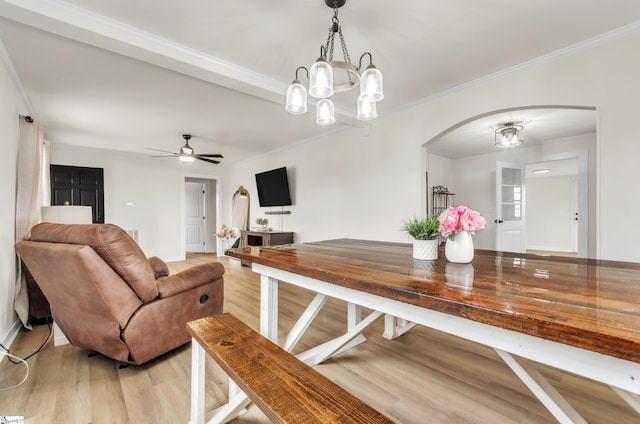 dining room with light wood-style flooring, ornamental molding, ceiling fan with notable chandelier, arched walkways, and baseboards