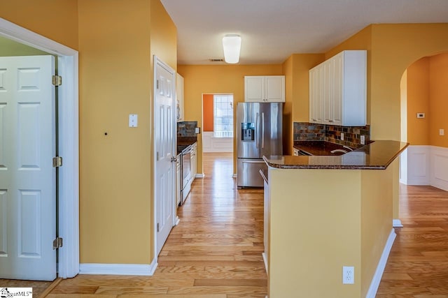 kitchen with light wood finished floors, dark stone counters, a peninsula, arched walkways, and stainless steel appliances