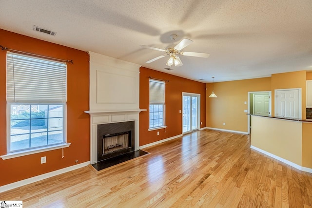 unfurnished living room featuring visible vents, light wood-style flooring, a textured ceiling, a large fireplace, and ceiling fan