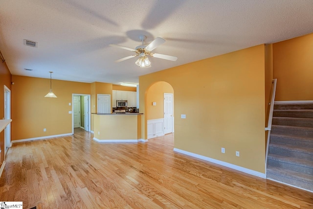 unfurnished living room featuring visible vents, arched walkways, ceiling fan, light wood-style floors, and a textured ceiling