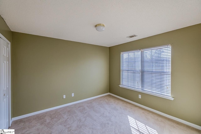 spare room with light colored carpet, baseboards, visible vents, and a textured ceiling