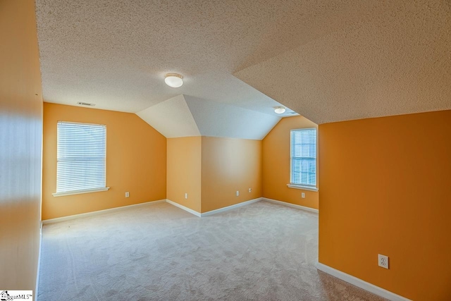 additional living space with visible vents, baseboards, carpet floors, lofted ceiling, and a textured ceiling