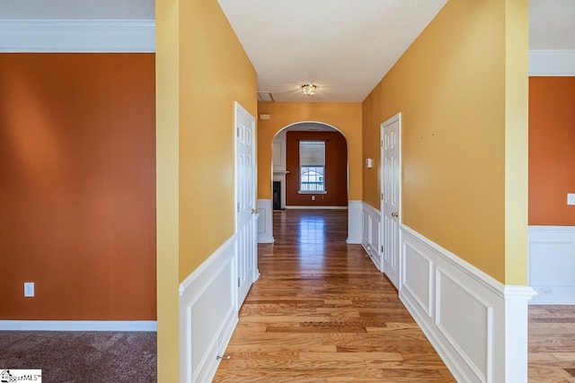 hallway featuring a wainscoted wall, a decorative wall, light wood-style floors, and arched walkways