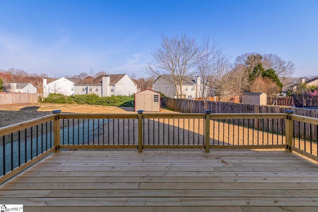 wooden deck featuring a storage shed, a fenced backyard, a residential view, and an outdoor structure