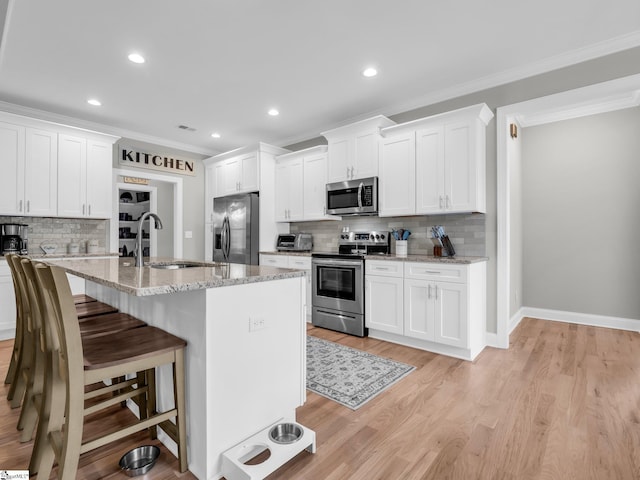 kitchen featuring a breakfast bar, ornamental molding, light wood-style flooring, stainless steel appliances, and a sink