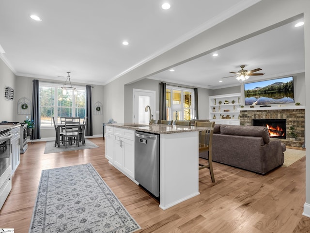 kitchen featuring ornamental molding, a sink, appliances with stainless steel finishes, white cabinets, and a brick fireplace