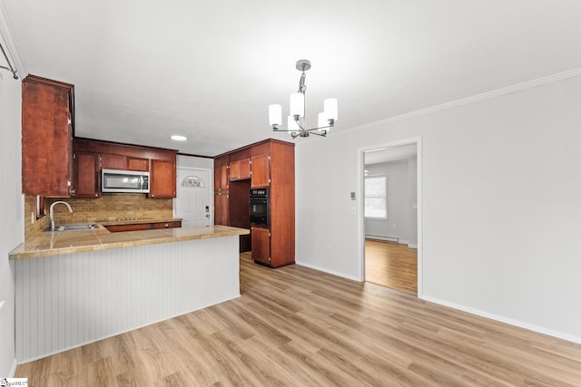 kitchen with a peninsula, a sink, decorative backsplash, black appliances, and a notable chandelier