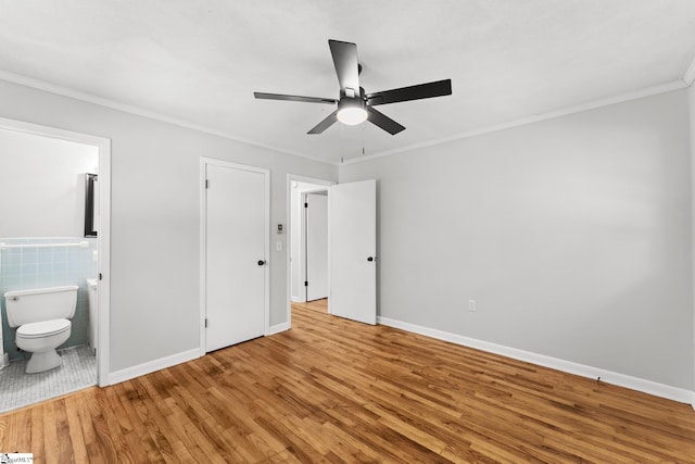 unfurnished bedroom with wood finished floors, baseboards, ensuite bath, crown molding, and tile walls