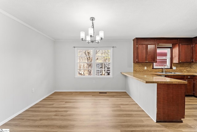 kitchen featuring a peninsula, a sink, a notable chandelier, light wood-type flooring, and backsplash