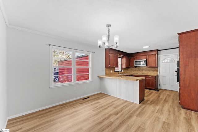 kitchen featuring an inviting chandelier, a peninsula, a sink, light countertops, and stainless steel microwave