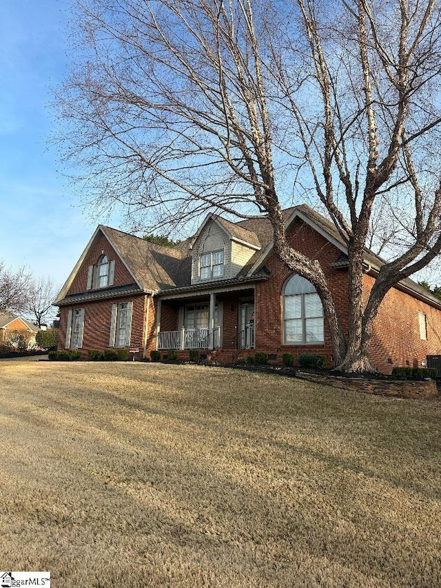 view of front of house featuring brick siding, covered porch, and a front lawn