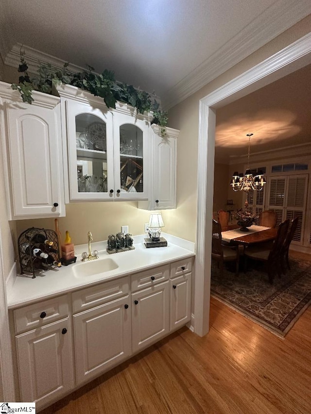 bar featuring pendant lighting, light wood-style flooring, a sink, an inviting chandelier, and crown molding