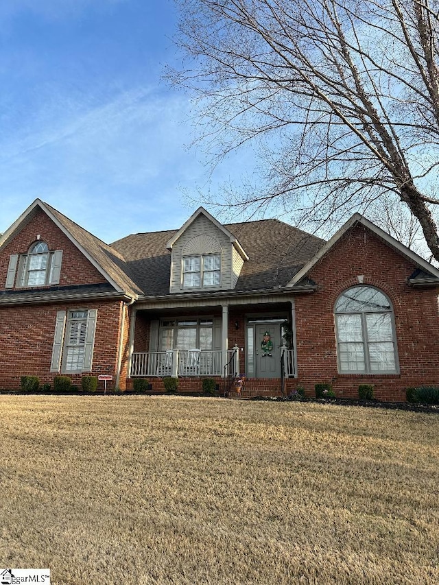 view of front of home featuring a front yard, a porch, brick siding, and a shingled roof