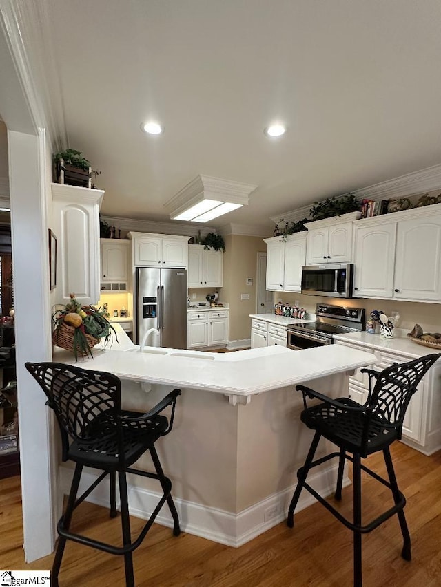 kitchen with crown molding, a kitchen breakfast bar, light wood finished floors, and appliances with stainless steel finishes