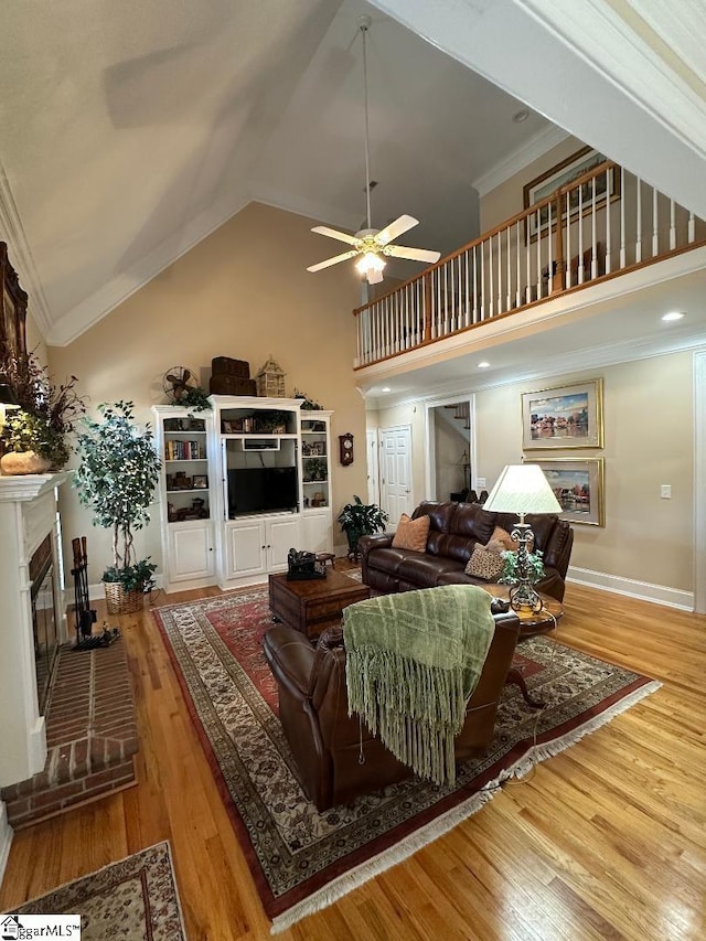 living room featuring wood finished floors, high vaulted ceiling, a fireplace, ceiling fan, and crown molding