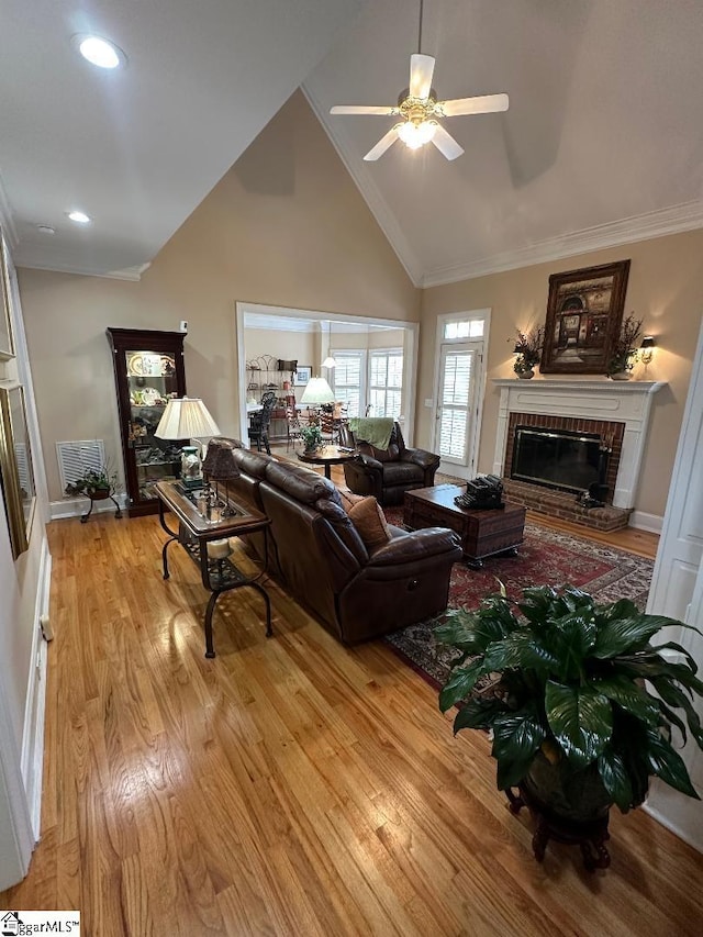 living room with light wood finished floors, crown molding, a fireplace, high vaulted ceiling, and a ceiling fan