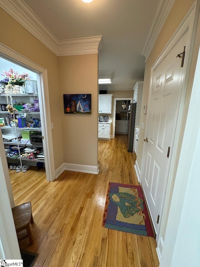 corridor featuring visible vents, baseboards, light wood-style floors, and ornamental molding