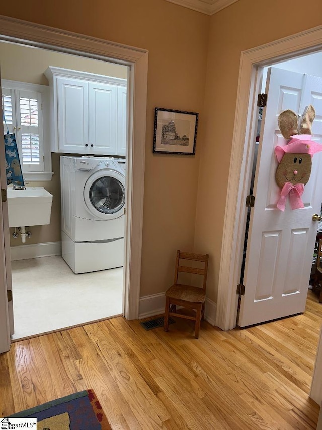 washroom featuring visible vents, baseboards, washer / clothes dryer, cabinet space, and light wood-type flooring