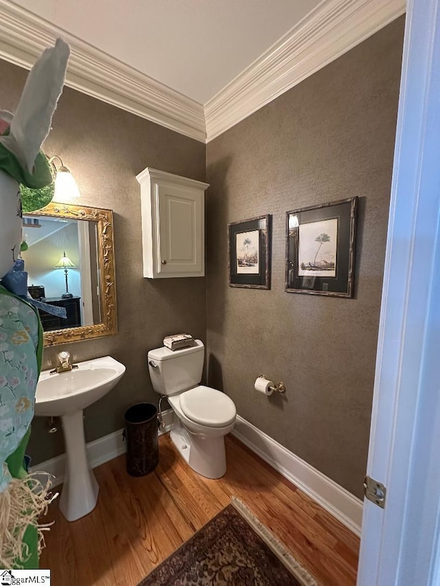 half bath featuring toilet, wood finished floors, baseboards, and ornamental molding