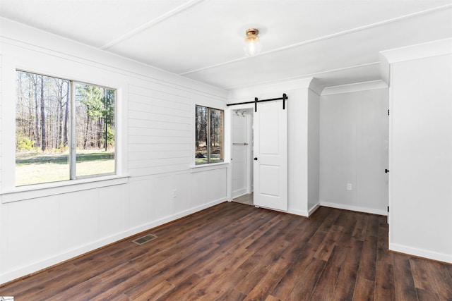 unfurnished bedroom featuring dark wood-style floors, visible vents, multiple windows, and a barn door