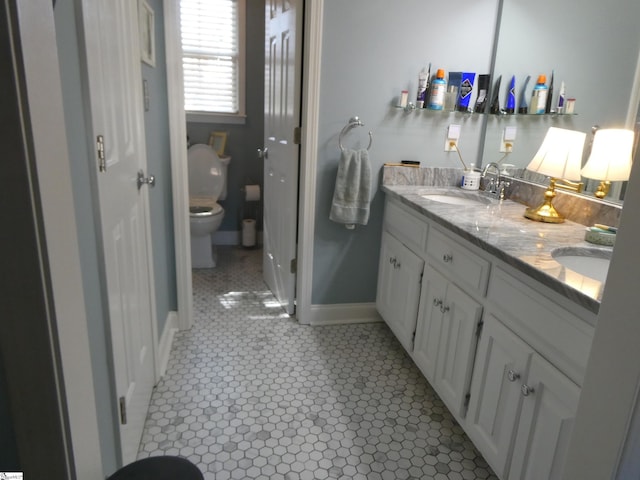 bathroom with double vanity, toilet, baseboards, and a sink