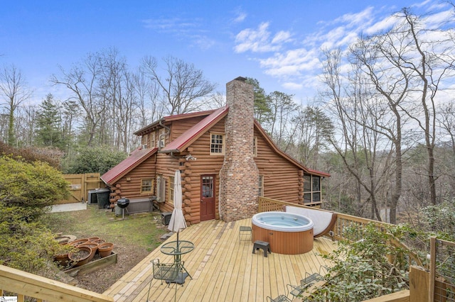 exterior space featuring fence, a wooden deck, log siding, a chimney, and a hot tub