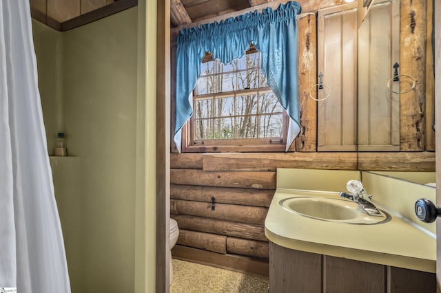 bathroom with toilet, log walls, and vanity